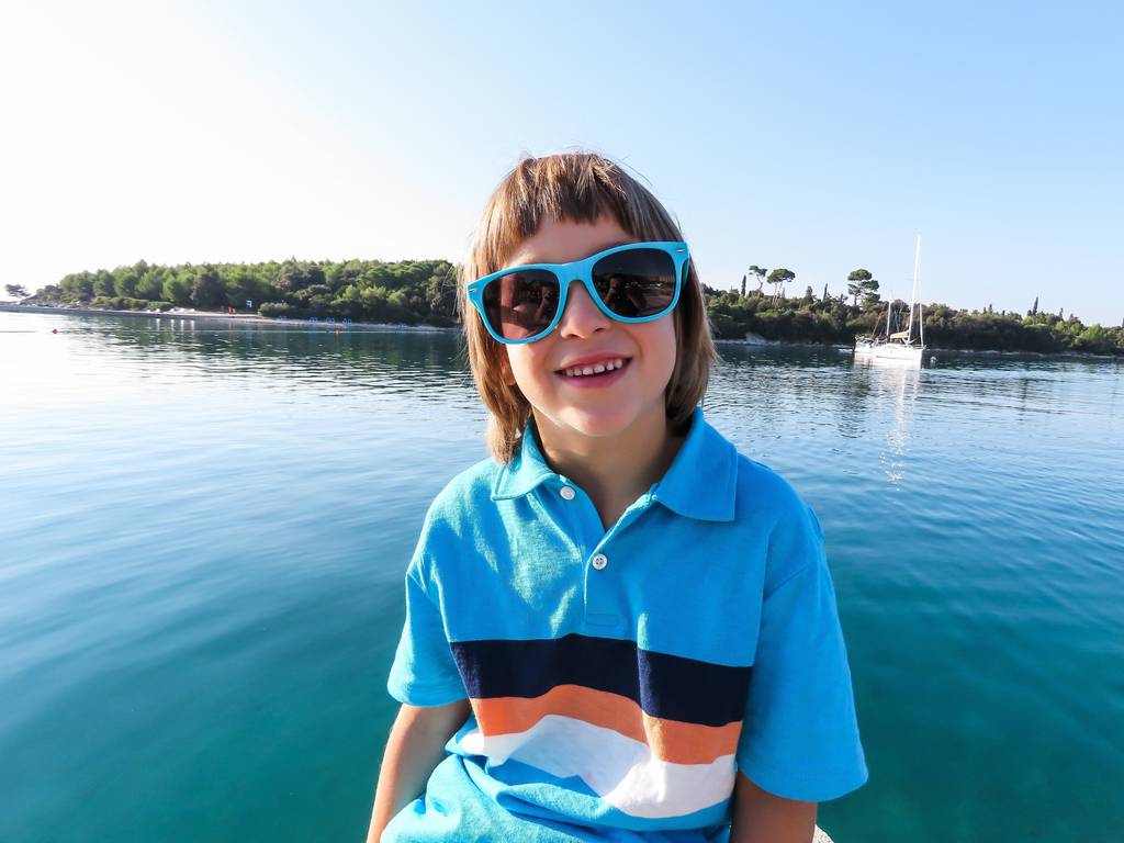 young boy smiling in the sun wearing sunglasses