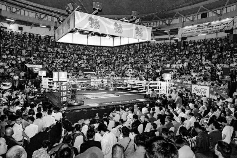 Muay Thai ringini çepeçevre saran, tribünleri doldurmuş büyük seyirci kalabalığının geniş açı siyah-beyaz fotoğrafı