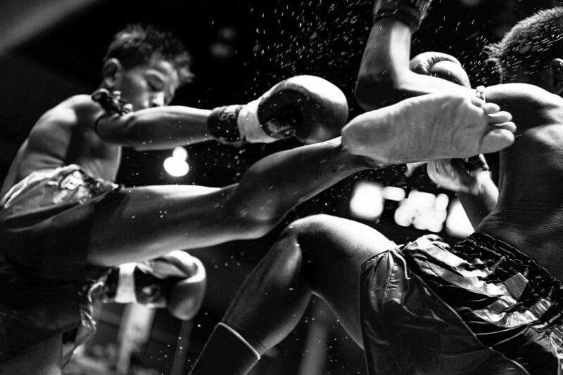 Muay Thai karşılaşmasında rakibine tekme atan sporcunun ve savunma yapan dövüşçünün yakın plandan siyah-beyaz fotoğrafı