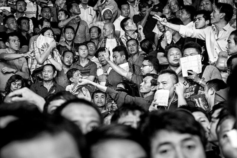 Muay Thai stadyumunun sıkışık tribünlerinde elleriyle işaretleşen ve kâğıt tutan seyirciler