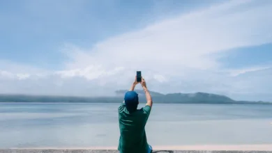 Seyahat fotoğrafçılığı için hangi mobil aksesuarlar iyidir? 21 person sits on wall in front of water while holiding up their phone