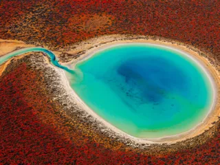 a turquoise body of water is surrounded by red earth