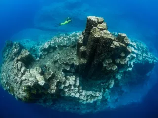 columns of basalt stick out of blue water with diver above