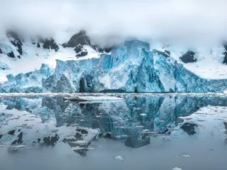 icy cliffs shrouded in clouds loom over iceburg filled water