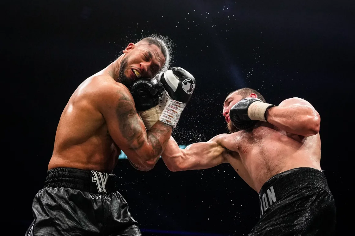 a boxer strikes the face of his opponent sending sweat spraying everywhere
