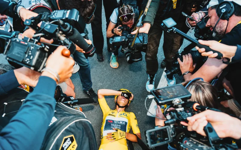 a cyclist is collapsed on the ground with a crowd of cameras hovering over her