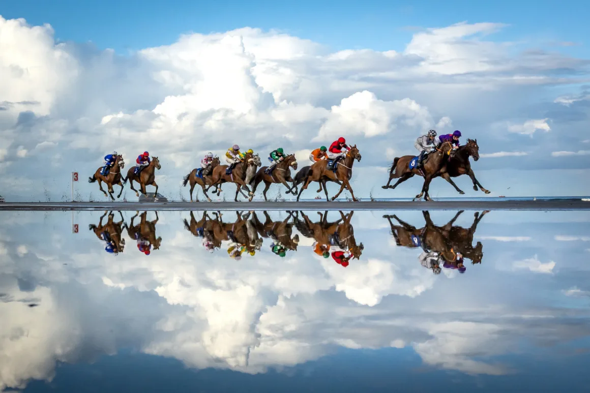 a group rides horses along a reflective pool of water