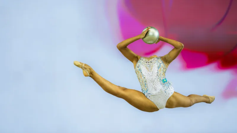 a gymnast wearing a white sparkling unitard leaps in the air