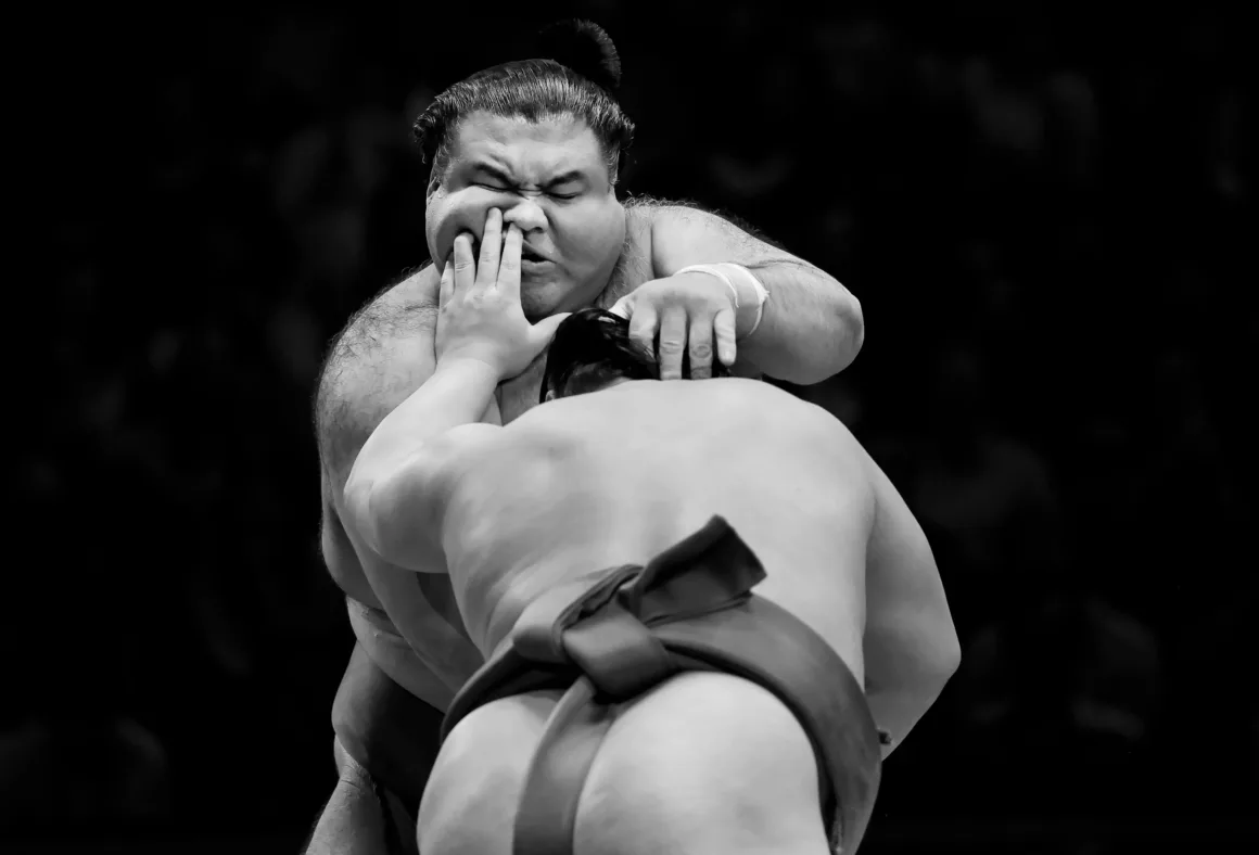 a man pushes on the face of hos sumo opponent