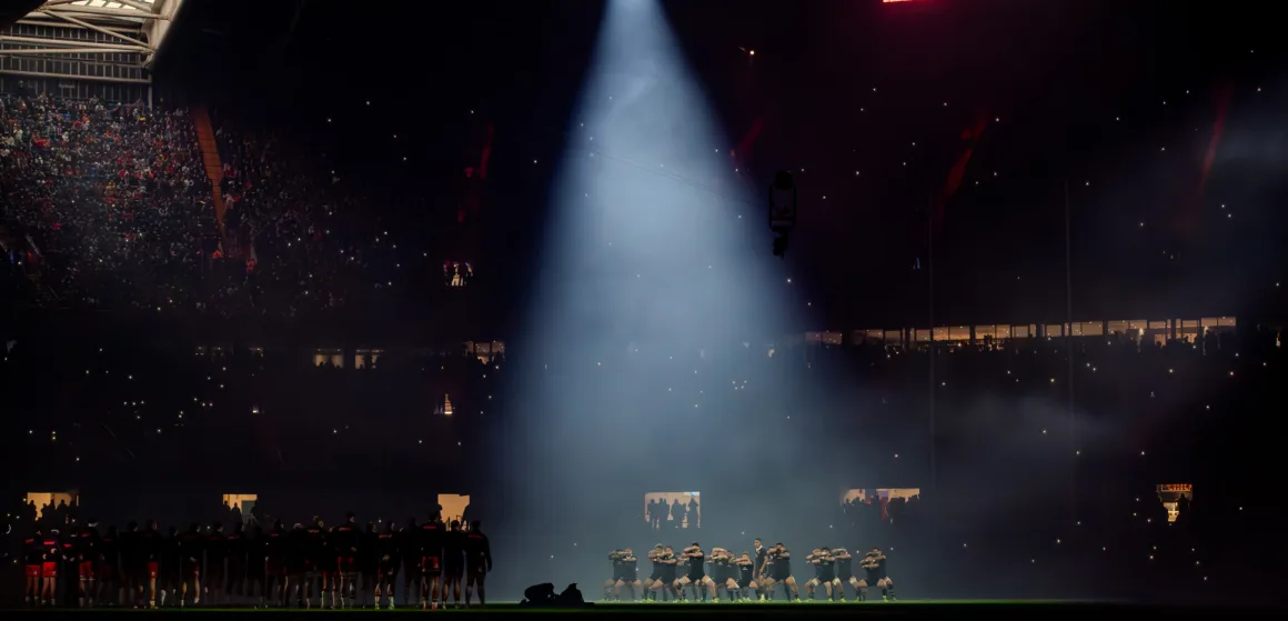 a rugby team performs a haka in an illuminated stadium