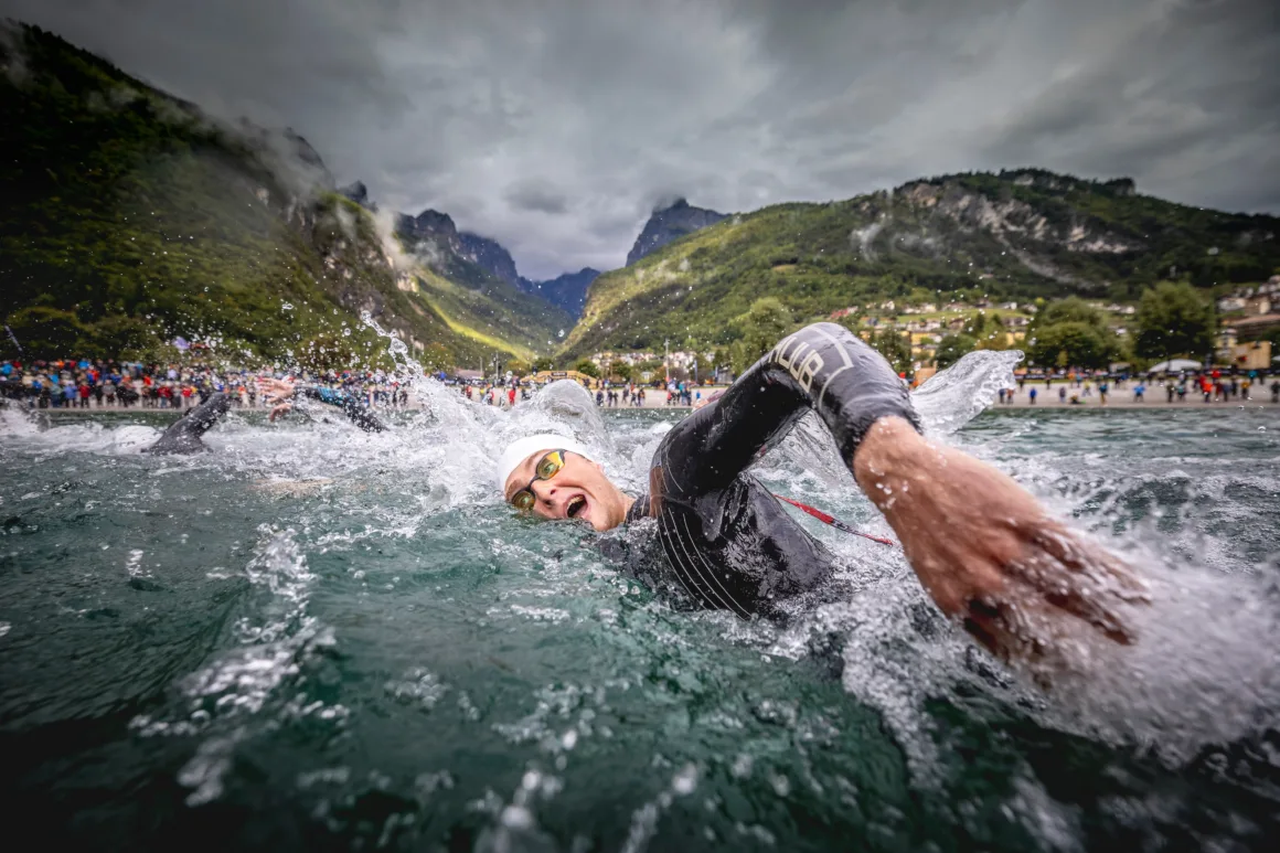 a swimmer takes a breath while swimming in an open body of water with mountains in the distance