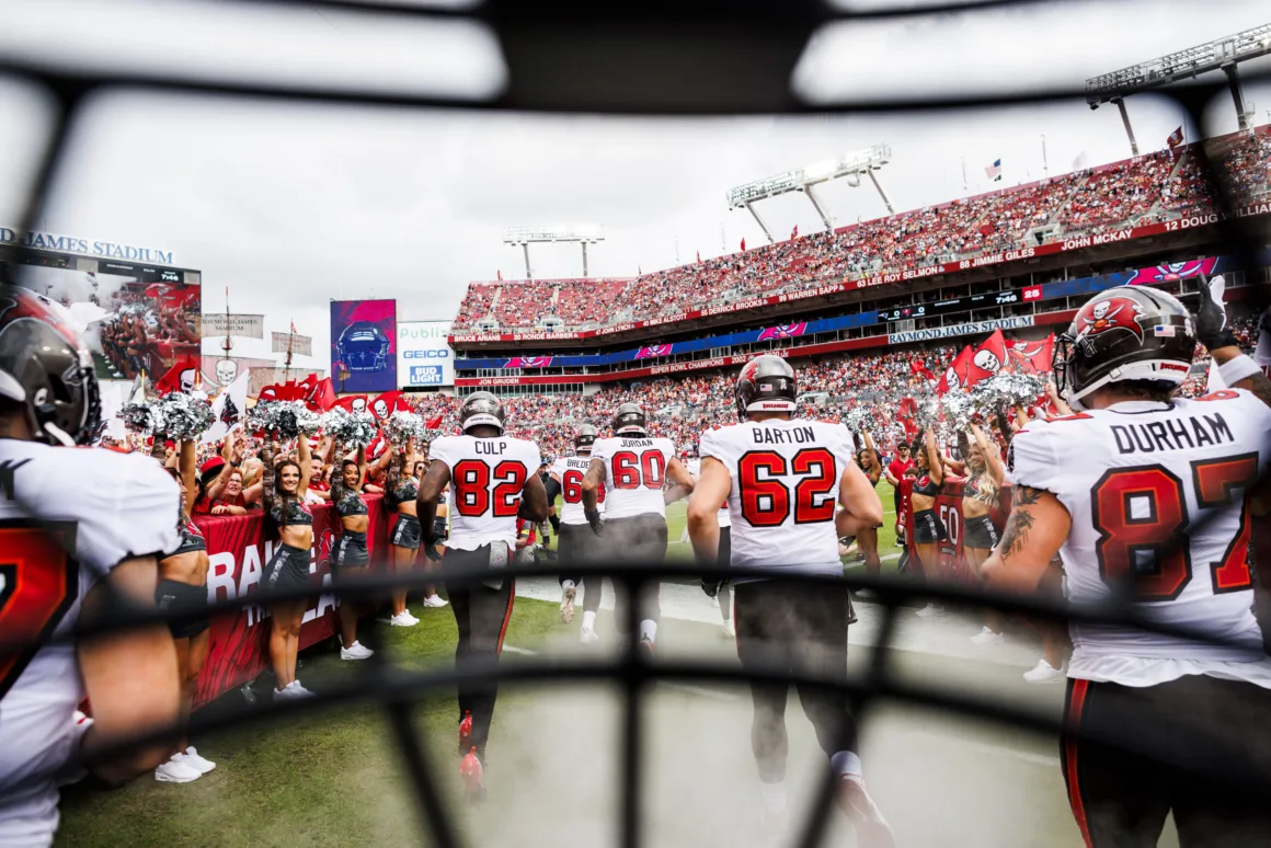 football players run onto a field with a helmet framing the view