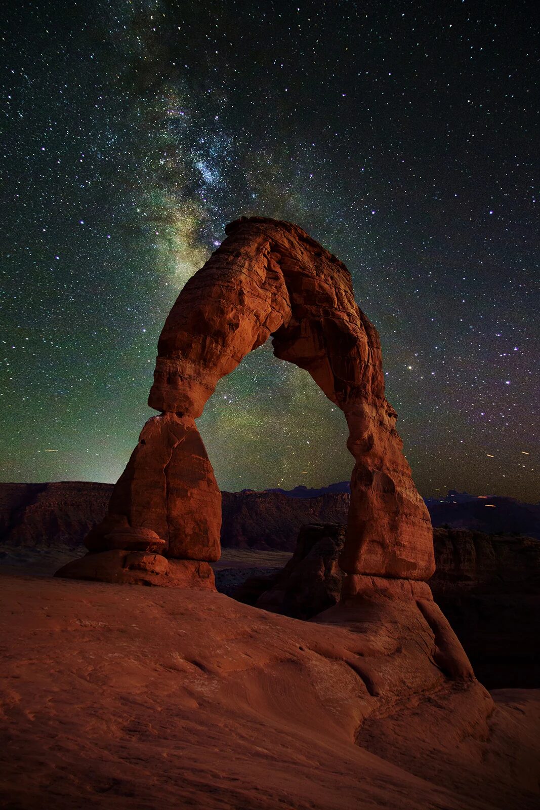 Delicate Arch in Arches National Park stands illuminated under a clear night sky filled with stars and the Milky Way, creating a dramatic and breathtaking natural scene.