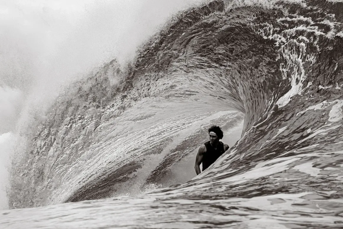 Güçlü bir dalganın tüpünün içinde ilerleyen sörfçünün siyah-beyaz çekimde dramatik şekilde kadrajlandığı an.