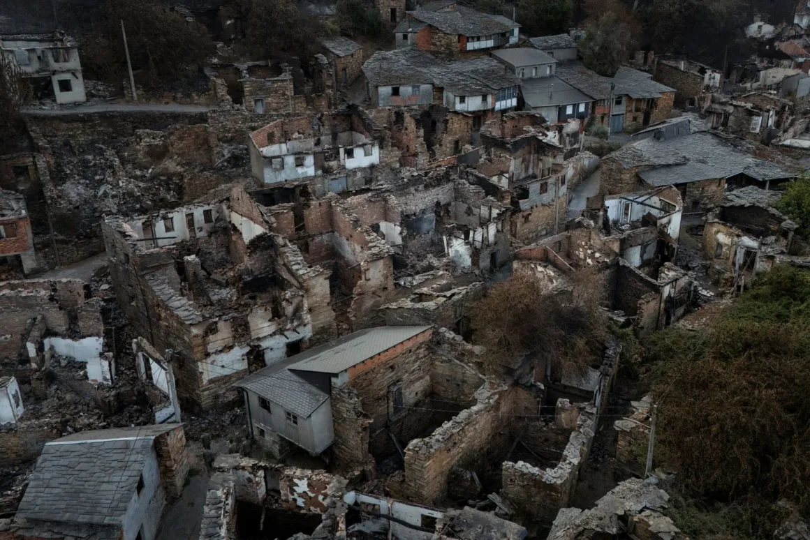 Çok sayıda evin ağır hasar gördüğü ya da yıkıldığı bir köyün havadan görünümü; çökmüş çatılar, yanmış duvarlar ve enkaz, bir yangın ya da felaketin ardından kalan izleri gösteriyor. Bazı yapılar kısmen ayakta.