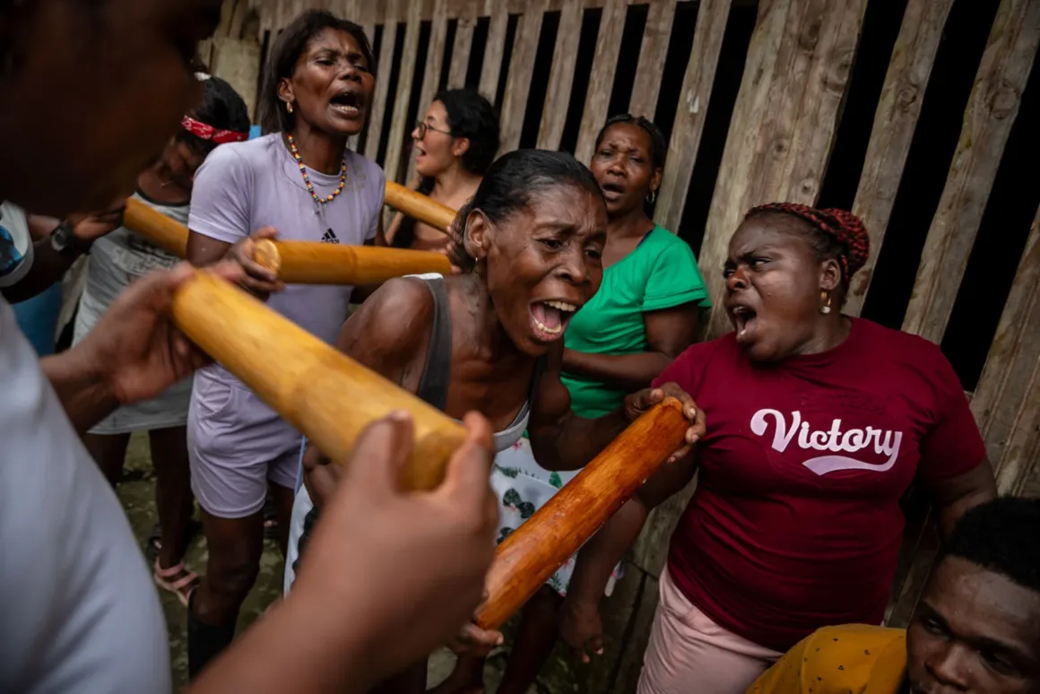 Bir grup kadın, bazıları tutkuyla şarkı söyleyerek ve ellerinde tahta sopalar tutarak, bir ahşap çitin yakınında duygularını güçlü şekilde ifade ederek bir araya gelmiş. Ön planda “Victory” yazılı tişört giyen bir kadın öne çıkıyor.