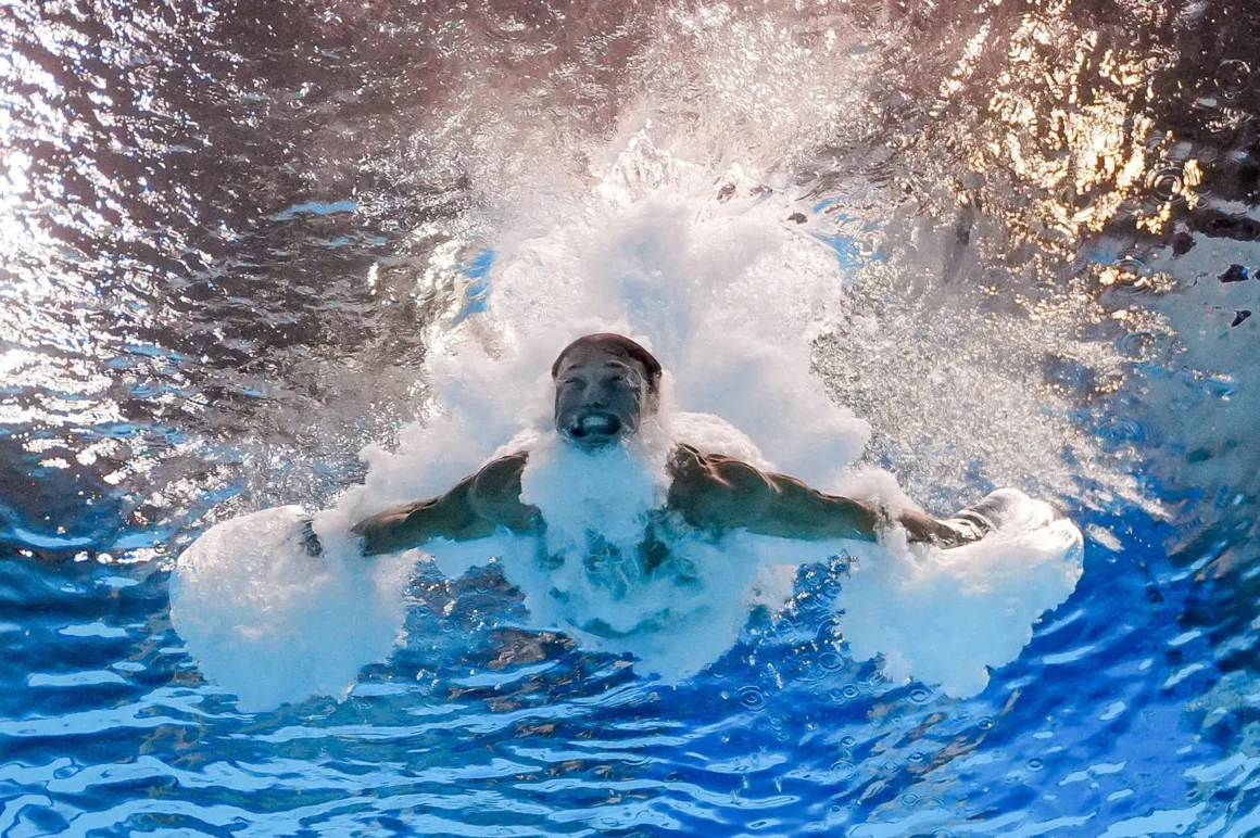 Suya dalış sonrası su altında kollarını açmış yüzücünün, kabarcıklar ve ışık yansımalarıyla çevrili etkileyici anı.