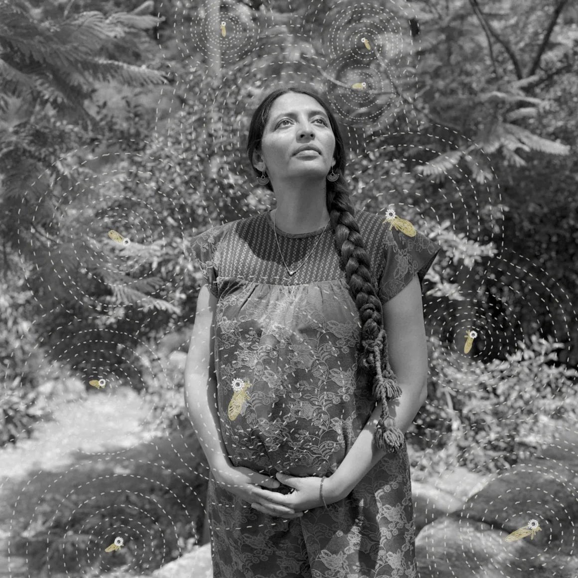 Uzun örgülü saçlara sahip bir kadın açık havada duruyor ve yukarı bakıyor. Hamile karnını tutuyor; etrafı sanatsal kesik çizgiler ve küçük illüstratif arılarla çevrili. Arka planda yumuşak ışık altında yapraklı ağaçlar yer alıyor.