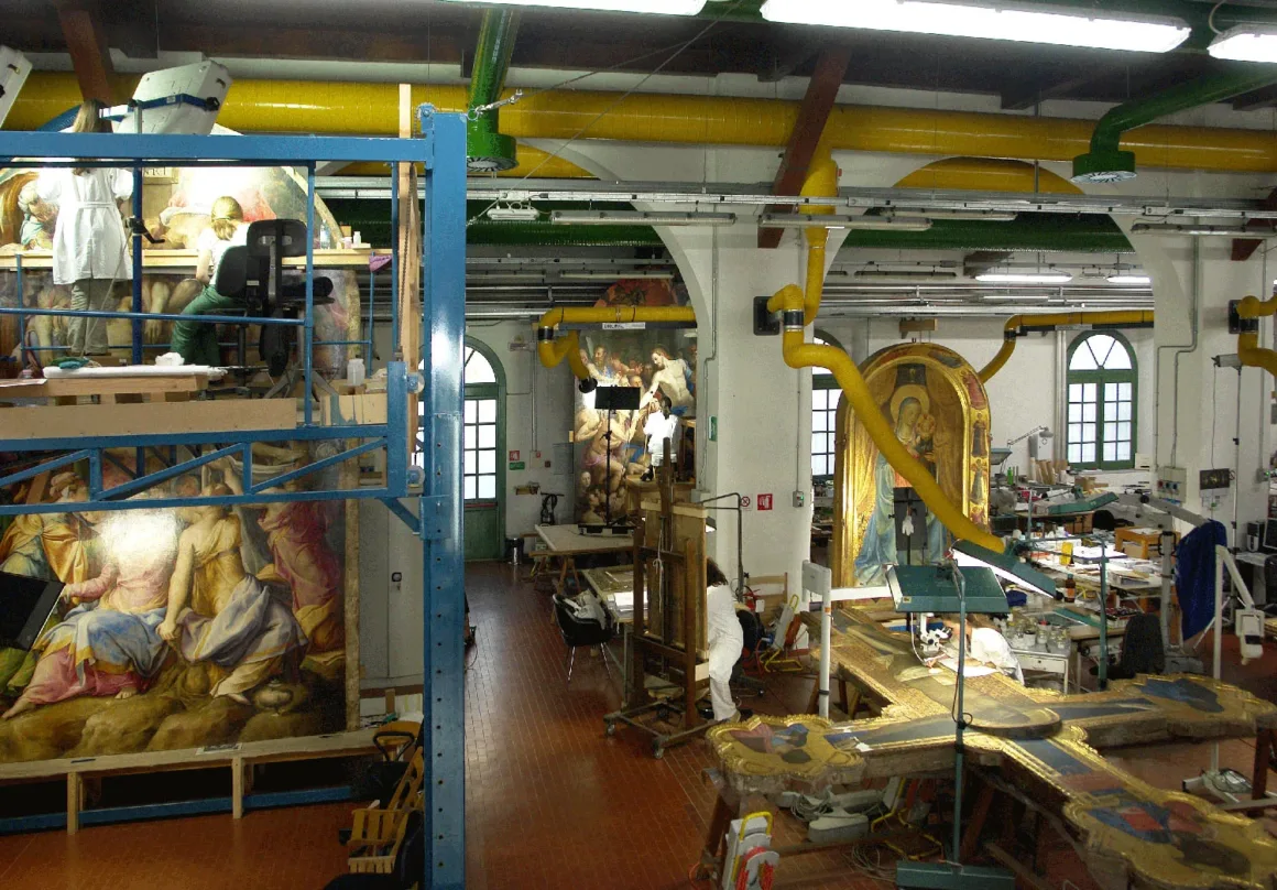 Yapay Zekâ ile Eski Fotoğrafları ‘Restore Etmek’ Temelden Hatalı Bir Yaklaşım 2 Large art restoration studio with high ceilings, filled with conservation equipment, large religious paintings, and artifacts being restored. Two people work on scaffolding and tables amid the artworks and restoration tools.