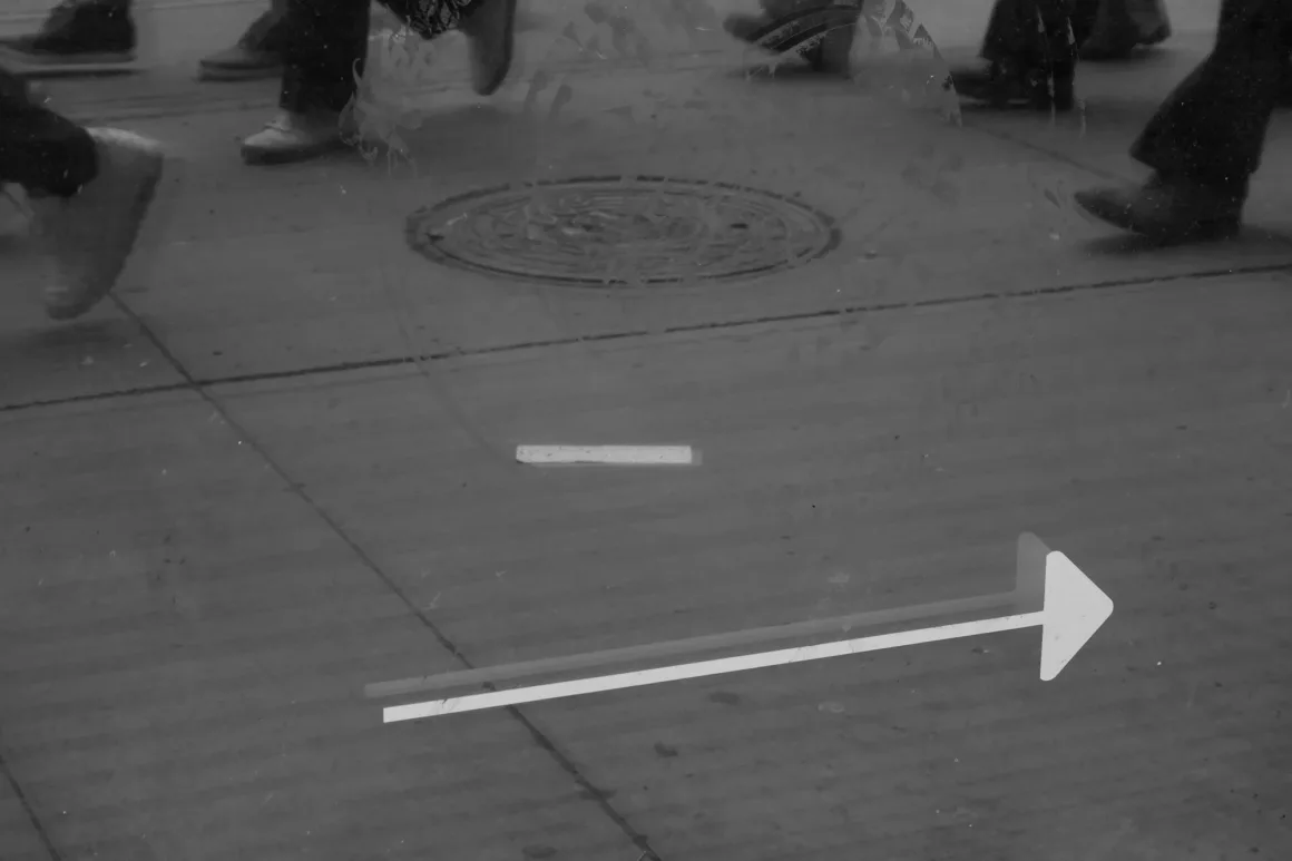 Panasonic Lumix ZS300 İnceleme: Eski Model Daha İyiydi? 24 Kaldırımda yürüyen bir grup insan, dizlerinden aşağısı görünecek şekilde kadrajlanmış. Zeminde sağa doğru yönü gösteren beyaz bir ok ve çizgi işareti bulunuyor. Görüntü siyah beyaz.