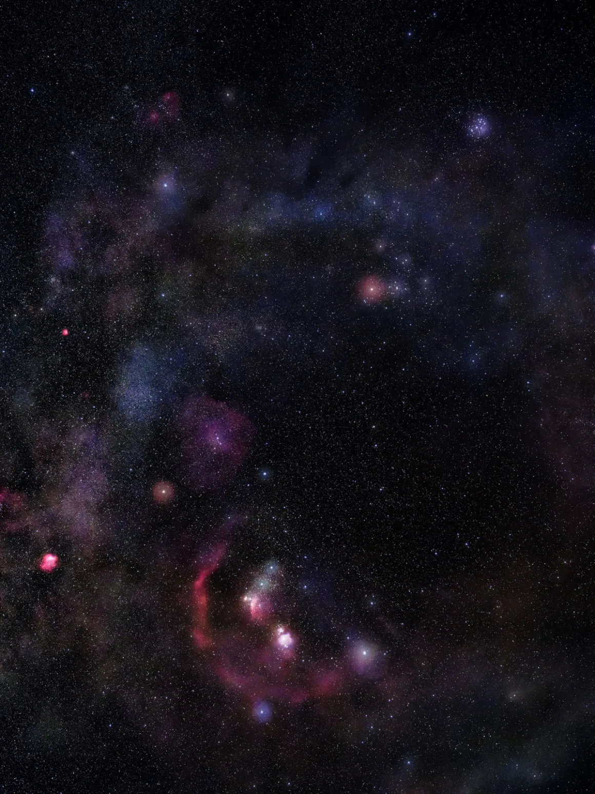 Canlı bir gece gökyüzünde yoğun bir yıldız alanı, kırmızı, mavi ve mor tonlarda parlayan renkli nebulalar ve yıldızlararası toz bulutlarıyla, uzayın karanlık fonunda belirgin şekilde görülüyor.
