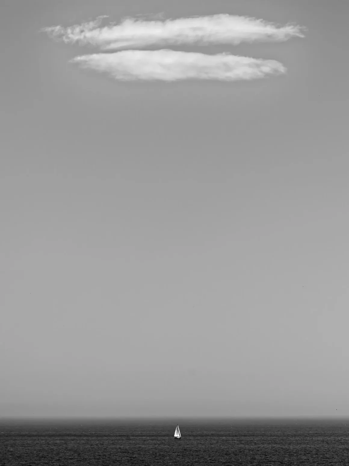 Fotoğrafçılar İçin Tasarım Neden Vazgeçilmezdir? 11 Ufukta tek bir yelkenlinin yer aldığı, geniş gökyüzü altında minimal siyah-beyaz bir deniz manzarası; üstte tek bir bulut bulunuyor.