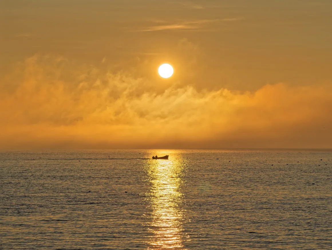 Fotoğrafçılar İçin Tasarım Neden Vazgeçilmezdir? 16 Altın saatlerde sakin su üzerinde yüzen küçük bir tekne; güneşin yansıması ve turuncu bulutlar sahneye yumuşak bir atmosfer katıyor.