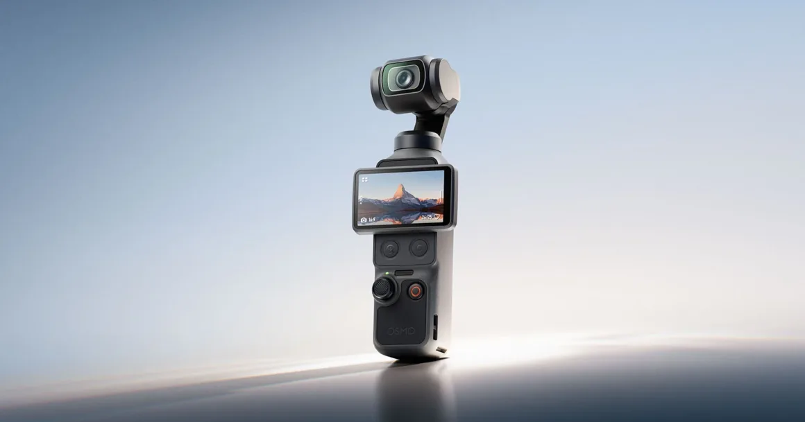 DJI Osmo Pocket 4 Tanıtıldı: 4Kp240 Video, Güçlü Fotoğraf Güncellemeleri
Dahili gimbala sahip kompakt bir el kamerası dik şekilde duruyor. Ekranında gün batımında dağların yer aldığı bir manzara görünüyor. Cihazın ön yüzünde birkaç düğme ve bir joystick bulunuyor. Arka plan yumuşak ışıkla aydınlatılmış ve minimal.