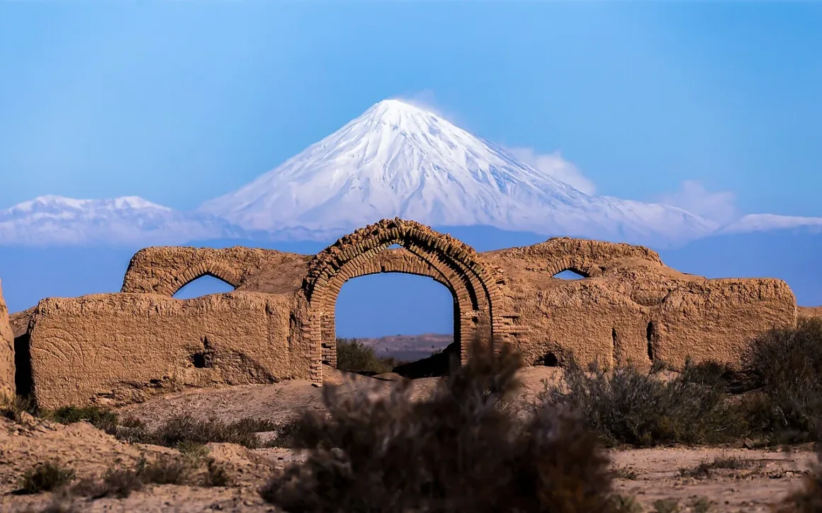 Wiki Loves Monuments Yarışmasının En İyi 10 Fotoğrafı
Kurak bir arazide, açık mavi gökyüzü altında yer alan kemerli geçide sahip eski ve yıpranmış tuğla kalıntıların arkasında yükselen karla kaplı bir dağ.