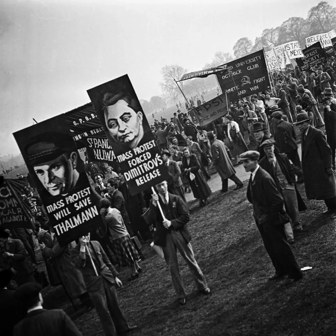 Büyük bir açık hava protestosunu gösteren siyah-beyaz bir fotoğraf. İnsanlar, üzerinde illüstrasyonlar ve “Kitle protestosu Thälmann’ı kurtaracak” ve “Kitle protestosu Dimitrov’un serbest bırakılmasını sağladı” gibi mesajlar bulunan pankartlar taşıyor.