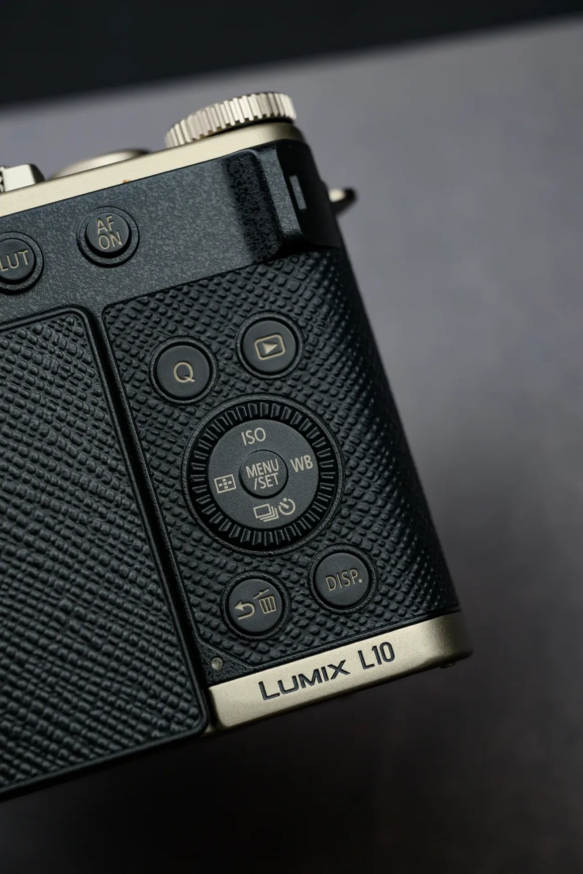 Panasonic Lumix L10 İncelemesi: Kompakt Kameraların Geri Dönüşü 11 Siyah ve altın renkli Panasonic Lumix L10 kameranın kontrol düğmeleri ve dokulu tutma alanının yakın plan görüntüsü. Menü tekeri, ekran düğmesi ve üst kadranların bir kısmı görülüyor.