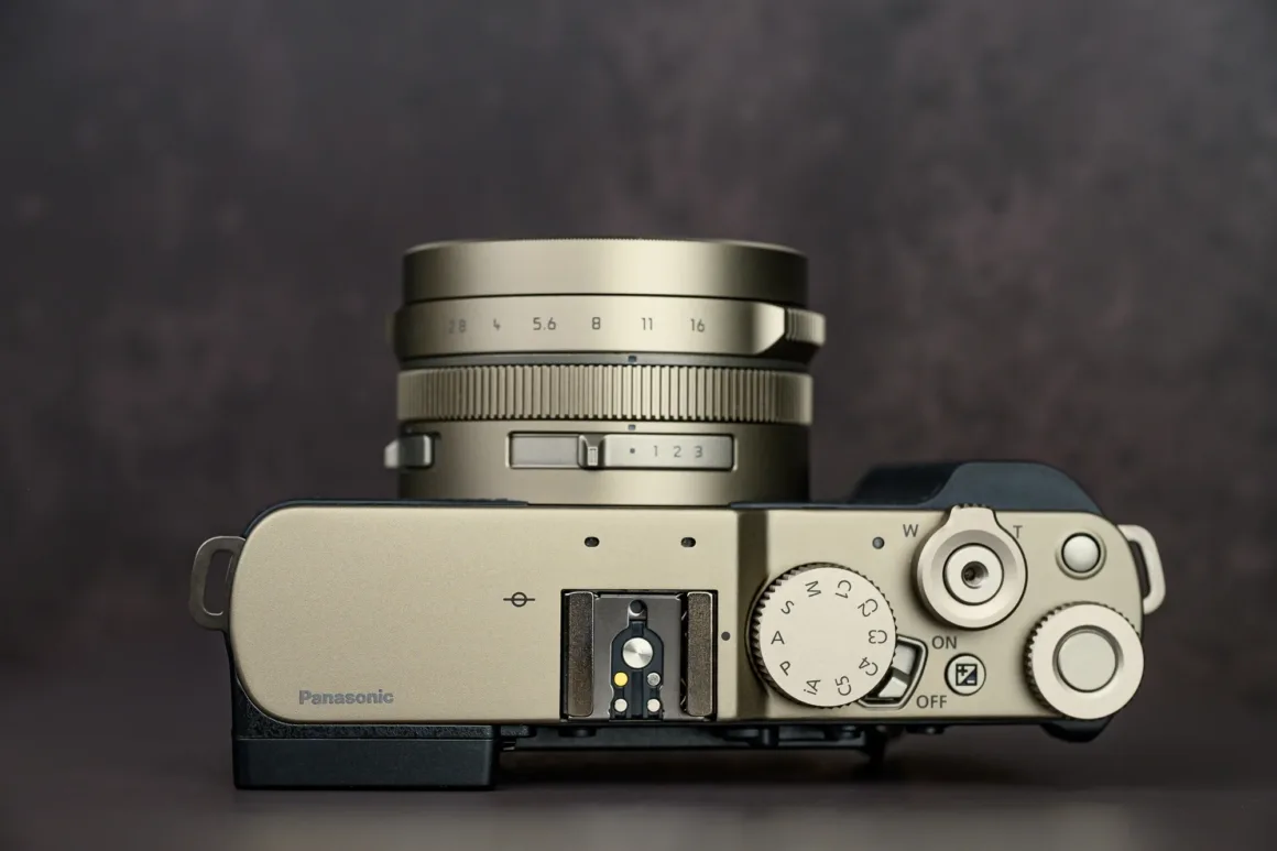 Panasonic Lumix L10 İncelemesi: Kompakt Kameraların Geri Dönüşü 10 Metalik kaplamalı Panasonic dijital kameranın üstten görünümü. Lens, düğmeler, kadranlar ve açma kapama anahtarı karanlık arka plan önünde görülüyor.