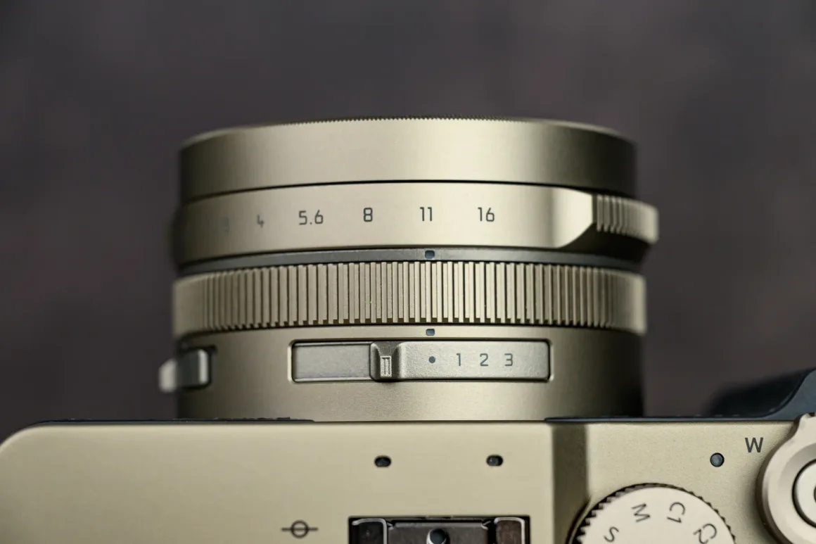 Panasonic Lumix L10 İncelemesi: Kompakt Kameraların Geri Dönüşü 5 Metalik kamera lensinin yakın plan görüntüsü. f/2 ile f/16 arasındaki diyafram değerleri, dokulu netleme halkası ve bej gövdedeki 1, 2, 3 yazılı anahtar görülüyor.