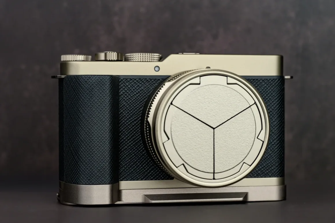 Panasonic Lumix L10 İncelemesi: Kompakt Kameraların Geri Dönüşü 1 Dokulu tutma alanına sahip modern gümüş ve siyah dijital kamera, karanlık ve bulanık bir arka plan önünde koyu bir yüzey üzerinde duruyor. Lensin üzerinde geometrik desenli dekoratif bir lens kapağı bulunuyor.