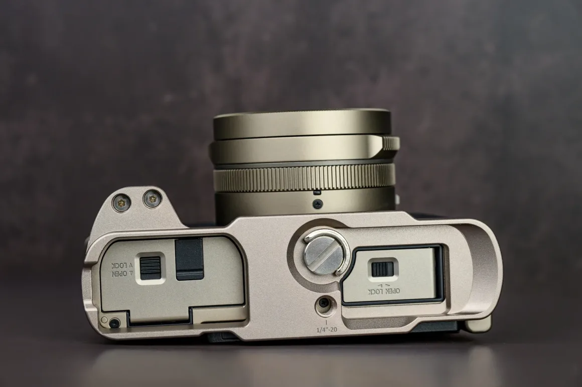 Panasonic Lumix L10 İncelemesi: Kompakt Kameraların Geri Dönüşü 12 Metalik kaplamalı kompakt dijital kameranın üst ve alt kısmının yakın plan görüntüsü. Lens, kontrol kadranları ve batarya ile hafıza kartı bölmeleri görülüyor.