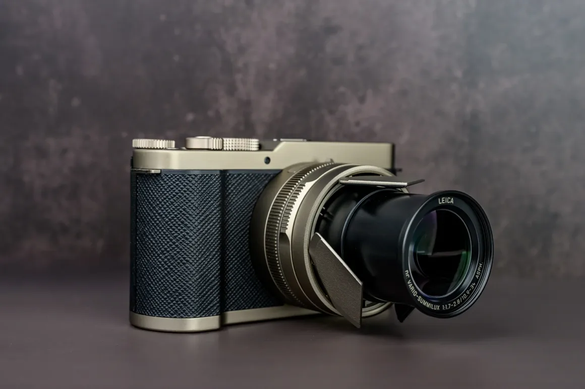 Panasonic Lumix L10 İncelemesi: Kompakt Kameraların Geri Dönüşü 3 Dokulu tutma alanına sahip gümüş ve siyah Leica kamera, uzatılmış zoom lensiyle düz bir yüzey üzerinde duruyor. Arka plan karanlık ve bulanık.