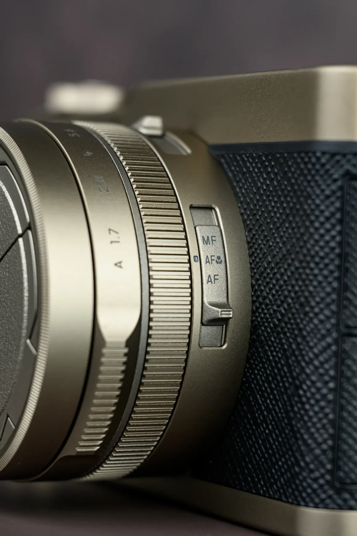 Panasonic Lumix L10 İncelemesi: Kompakt Kameraların Geri Dönüşü 18 Dokulu tutma alanına sahip kamera lensinin yakın plan görüntüsü. Üzerinde MF, AFS ve AF seçenekleri bulunan netleme modu anahtarı görülüyor. Gövde metalik detaylara sahip.