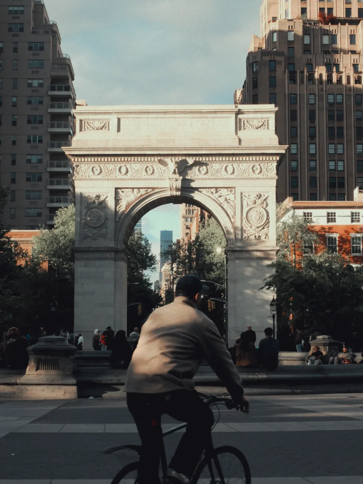 Kareden Önce: Bir Yönetmenin Sokak Fotoğrafçılığı Yaklaşımı 9 New York City’de Washington Square Arch önünden bisiklet süren bir kişi. Arka planda yüksek binalar, ağaçlar ve meydanda oturan ya da yürüyen insanlar görülüyor.