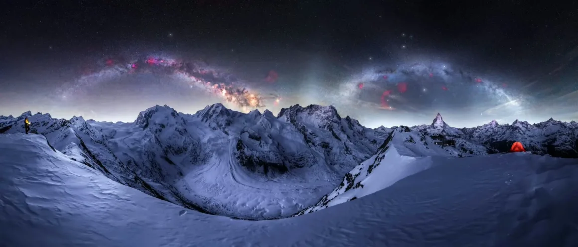 Yıldızlı gece gökyüzü altında karla kaplı dağların panoramik görüntüsü; solda sarı kıyafetli bir kişi, sağda ise parlayan turuncu bir çadır bulunuyor.