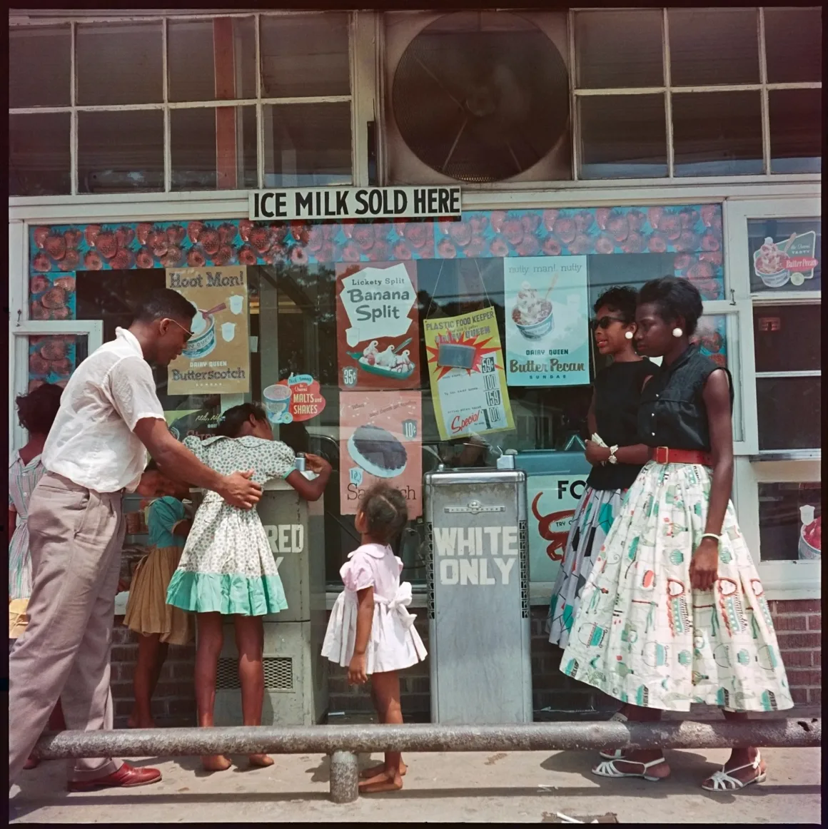 Gordon Parks’ın Segregation Story Fotoğrafları 70 Yıl Sonra Sergileniyor
Bir grup Siyah çocuk ve bir adam, girişin yanındaki camında "SADECE BEYAZLAR" yazan bir tabelanın bulunduğu dondurma dükkânının dışında duruyor. Çocuklar içeriyi izliyor gibi görünüyor.