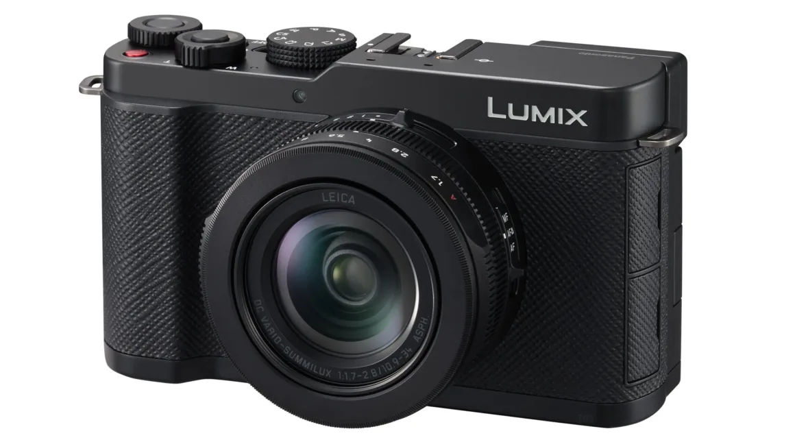 Leica lensli siyah Panasonic Lumix dijital kamera açılı şekilde gösteriliyor. Kameranın dokulu tutma alanı, üst bölümdeki düğmeleri ve kadranları görünür durumda. Büyük lens ön planda dikkat çekiyor.