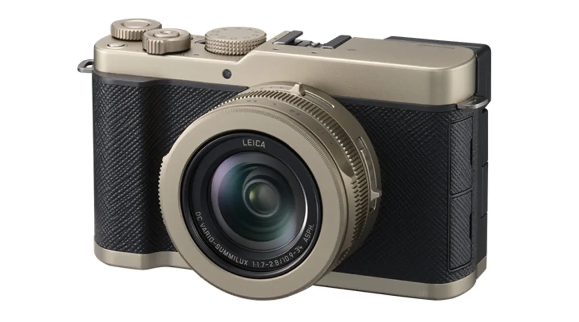 Büyük lensli, altın ve siyah renk kombinasyonuna sahip Leica dijital kamera. Kameranın dokulu tutma alanı ile üst bölümdeki düğme ve kadranları görünüyor. Kamera hafif sağ açıyla konumlandırılmış.