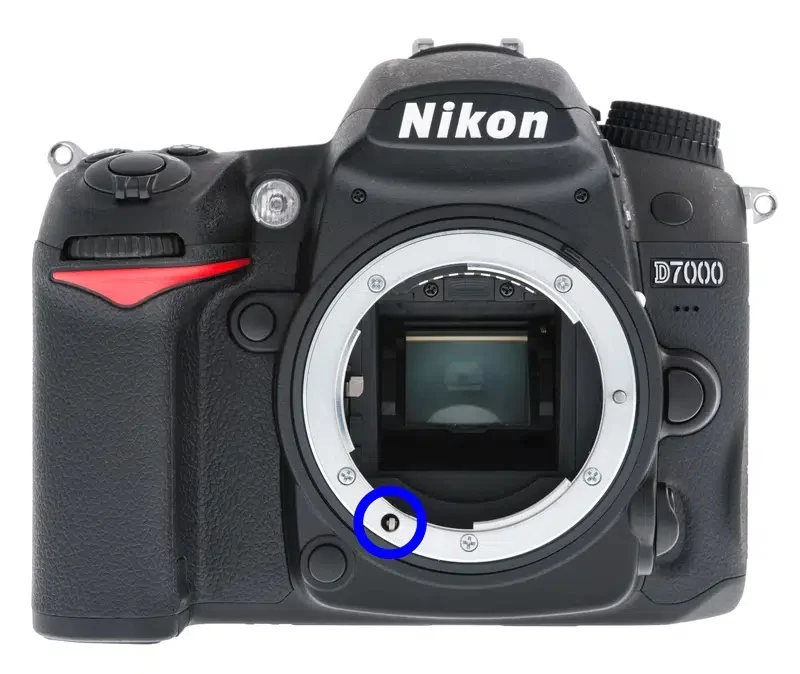 Lens takılmamış Nikon D7000 DSLR gövdesinin önden görünümü; lens yuvası ve mavi daire içine alınmış küçük metal sensör bağlantısı görülüyor.
