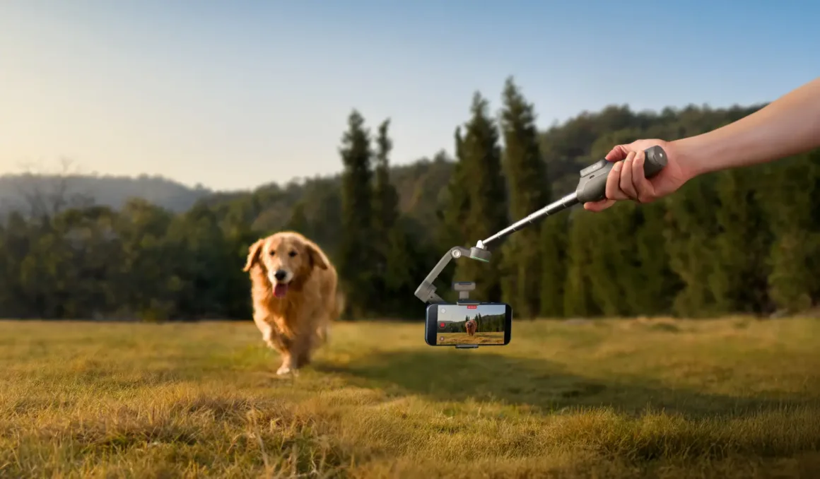 Bir kişi, gimbal üzerine yerleştirilmiş akıllı telefonla çimlik alanda koşan golden retriever köpeğini kaydediyor. Arka planda ağaçlar ve tepeler görülüyor.