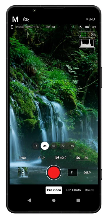 Bir akıllı telefon ekranında manuel modda çalışan kamera uygulaması görülüyor. Ekranda yemyeşil bir şelale manzarası yer alırken ISO, enstantane ve pozlama gibi kamera ayarları ile ortada büyük kırmızı kayıt tuşu bulunuyor.