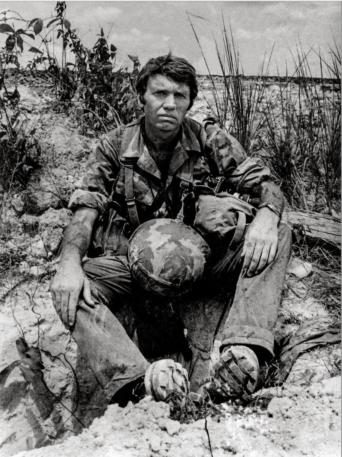 Don McCullin’in Son Fotoğraf Kitabı Vietnam’a Yaptığı 16 Yolculuğu Bir Araya Getiriyor 1 Don McCullin’in Son Fotoğraf Kitabı Vietnam’a Yaptığı 16 Yolculuğu Bir Araya Getiriyor
Kirli üniformasıyla yorgun bir asker, kum ve seyrek bitki örtüsü arasında yere oturmuş, kaskını dizlerinin üzerinde tutarken doğrudan kameraya bitkin bir ifadeyle bakıyor.
