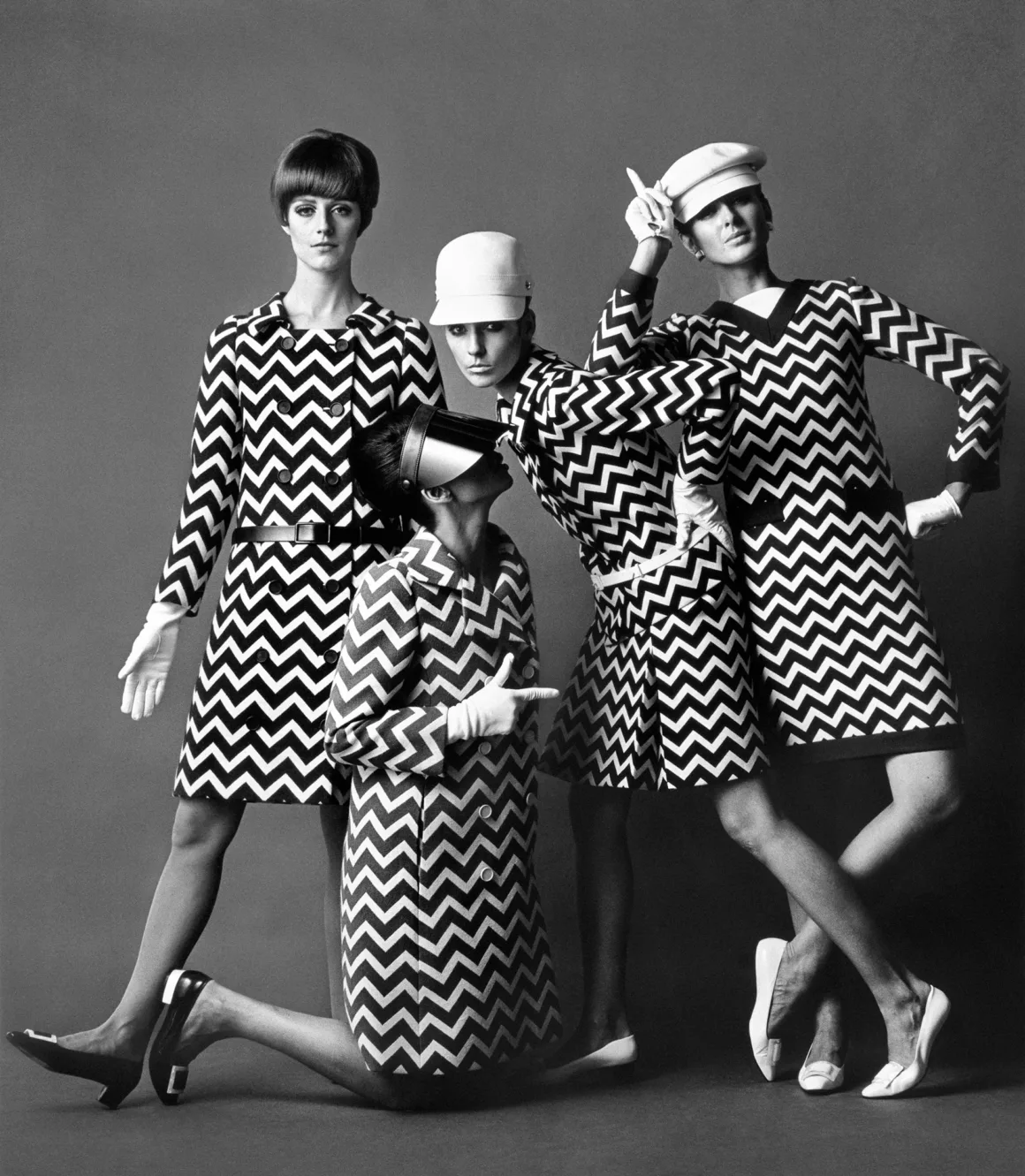 Yves Saint Laurent ve Fotoğraf: Bir Moda Efsanesini Şekillendiren 40 Yıl 2 Siyah beyaz moda fotoğrafında dört kadın, zikzak desenli uyumlu elbiseler ve şapkalarla sade bir arka plan önünde eğlenceli ve teatral pozlar veriyor.