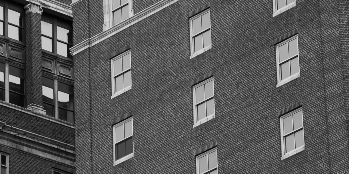 HiRezGo: Fotoğrafları Sıkıştırmadan Paylaşmanın Yeni Yolu 5 A black and white photo shows the exterior of a brick building with several windows, some open and some closed, alongside the corner of another older building with decorative trim and large, divided windows.