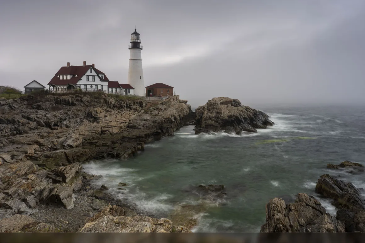 HiRezGo: Fotoğrafları Sıkıştırmadan Paylaşmanın Yeni Yolu 8 A lighthouse and adjacent buildings sit atop rocky cliffs overlooking a turbulent, misty sea under a cloudy sky. Waves crash against the rocks, and the scene appears calm yet dramatic.