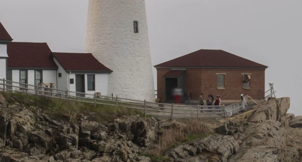 HiRezGo: Fotoğrafları Sıkıştırmadan Paylaşmanın Yeni Yolu 10 A lighthouse with a white tower and nearby brick and white buildings sits on rocky terrain, with several people standing near the entrance on a cloudy day.